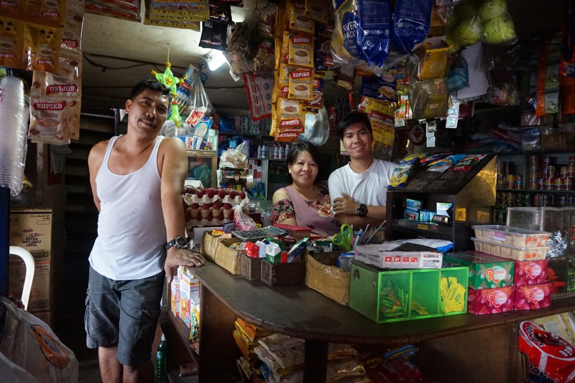 A father, mother, and son stand inside their convenience store.