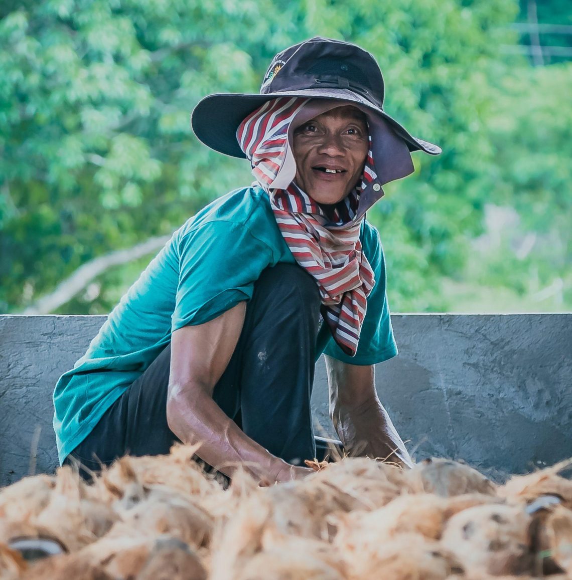 A man sits near a pile of coconuts and copra at a sorting and drying facility
