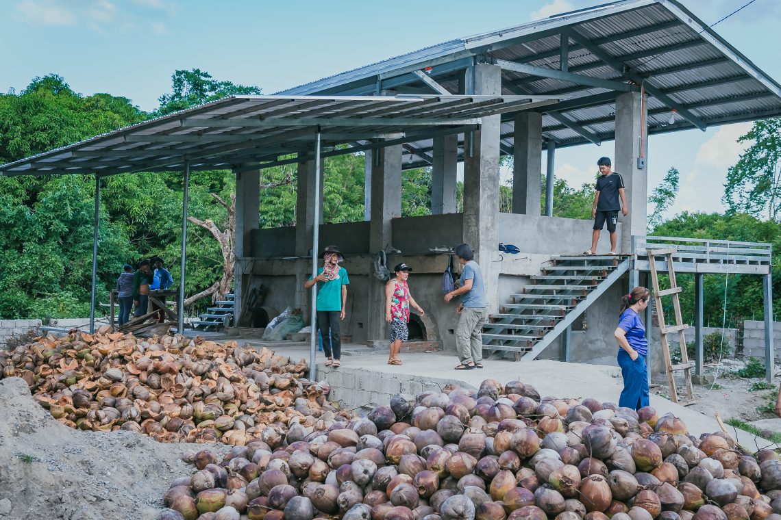 A group of men and women farmers walk around their coconut and copra sorting facility.