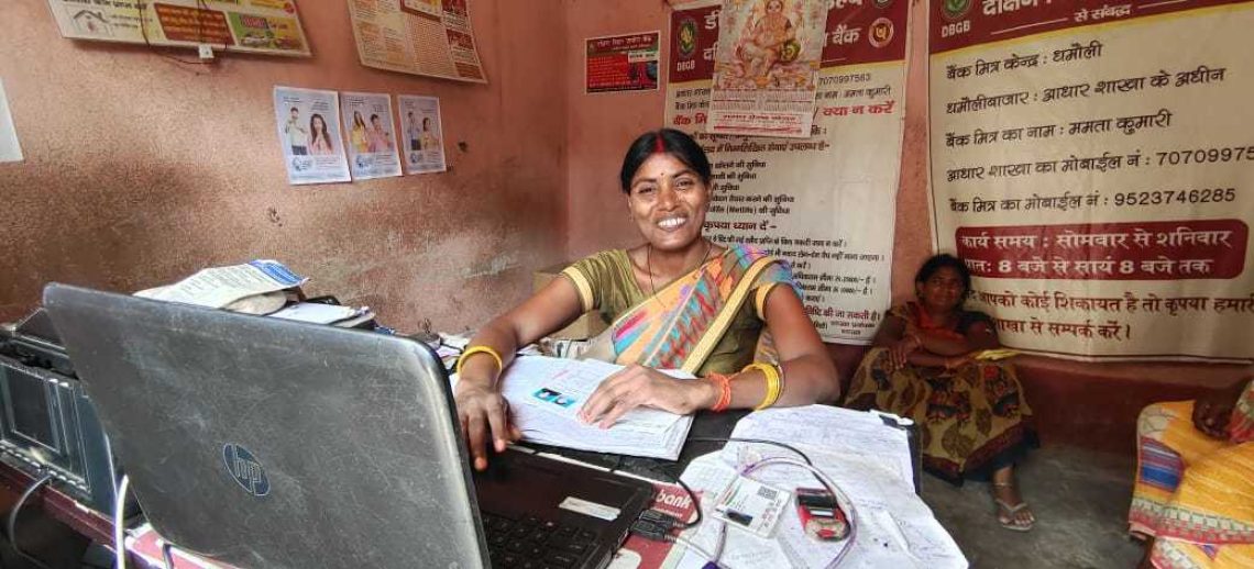 Malti, a Community Agent in Bihar, India, sits at her desk with a laptop. She is smiling at the camera.