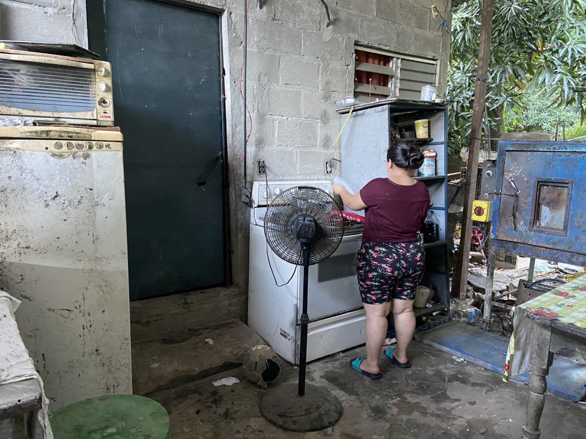 A woman stands with her back against the camera as she checks on banana bread in an outdoor oven