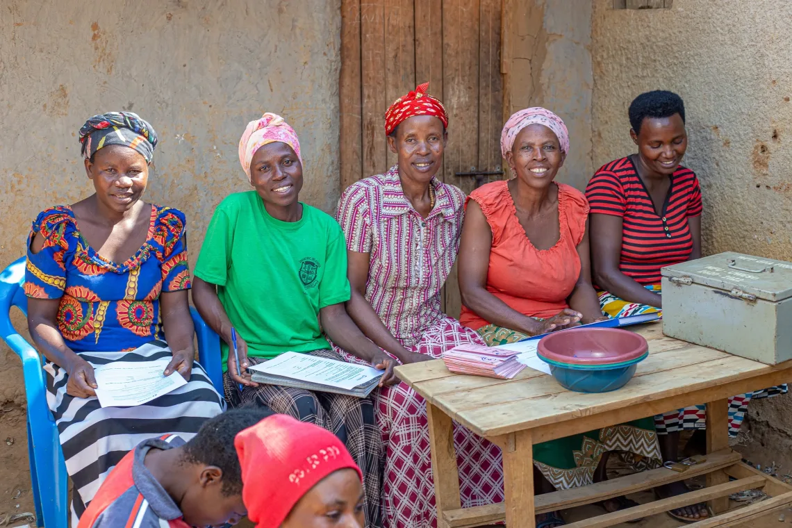 Grameen Foundation Refugee Finance Program supports women savings groups. This photos shows one of the savings group of five women seated at a table outside.
