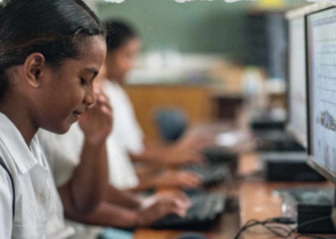 A young girl is seated at a computer with her hands on the keyboard