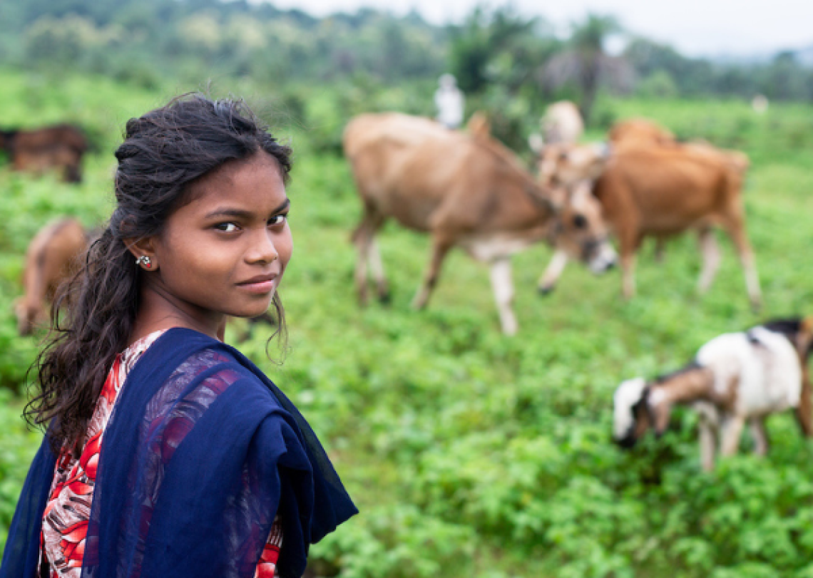 A young woman is standing in a field of tall grass and is looking back at the camera.