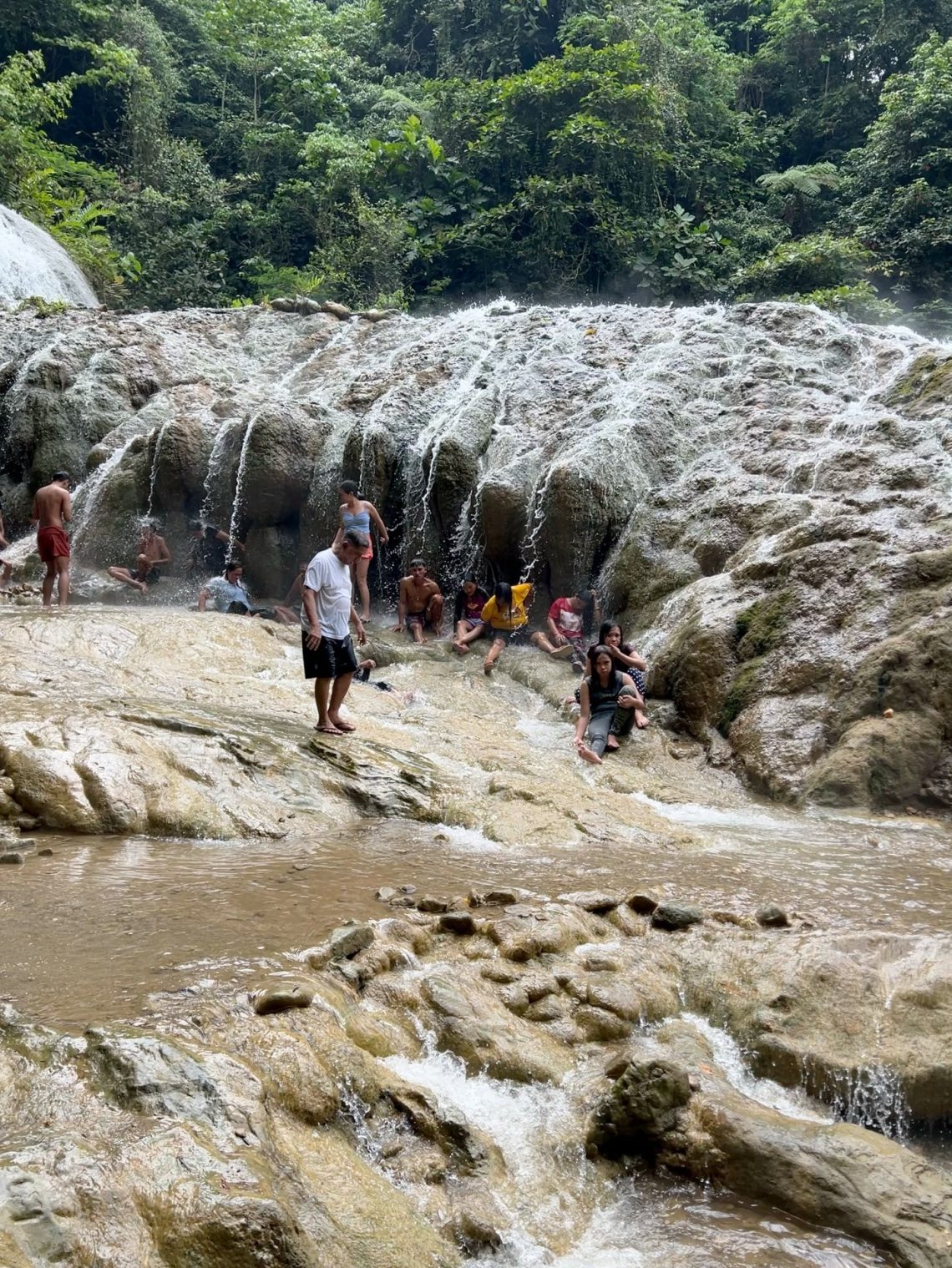 People sitting and standing in waterfall hotsprings