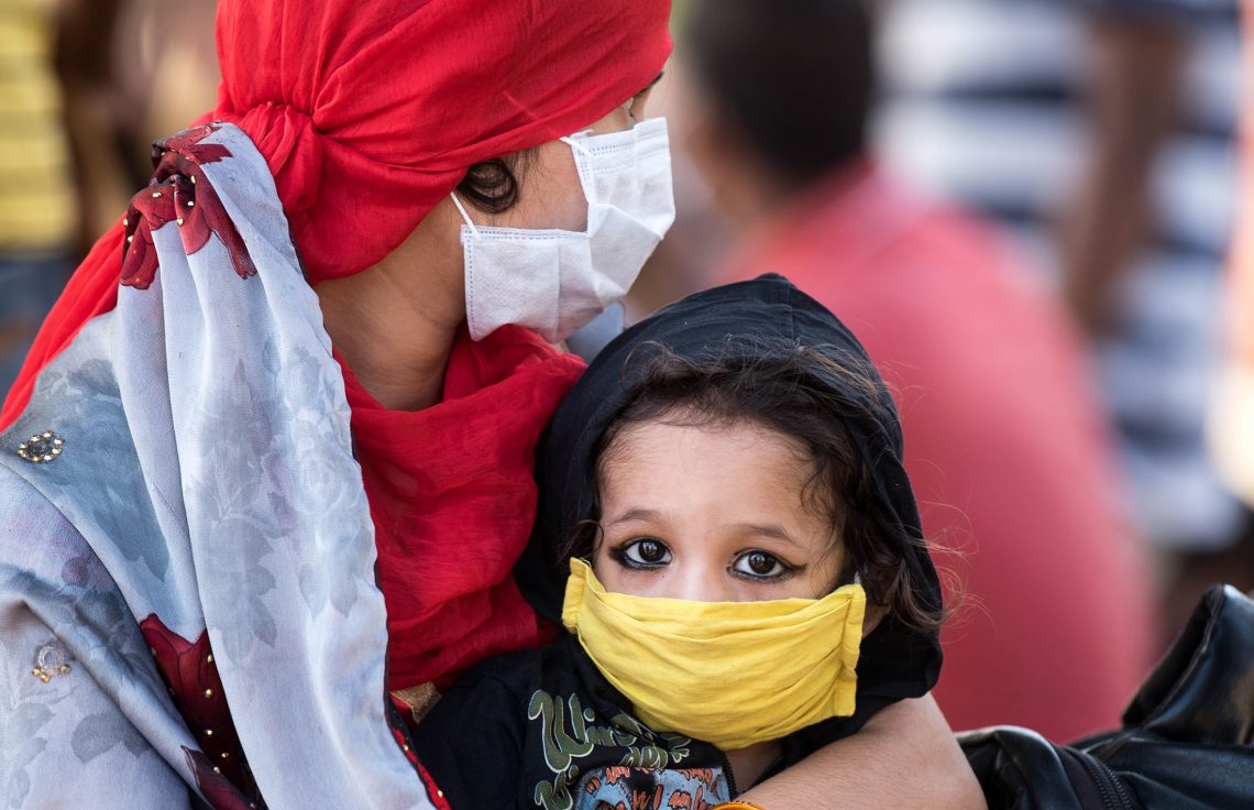 A woman wearing a mask holds her child, also wearing a mask, in Mumbai, India.