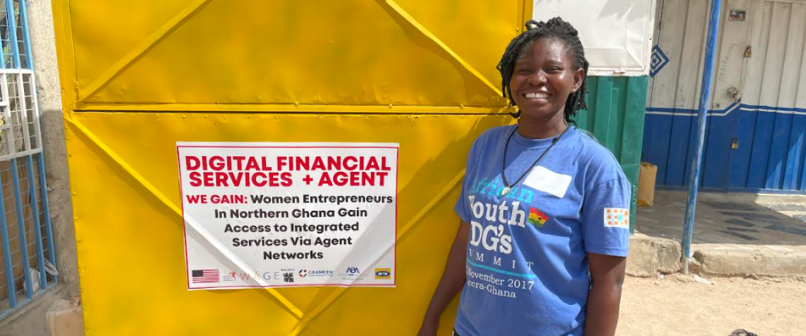 Grameen Foundation partner, Patience stands in front of her Grameen Agent booth in northern Ghana