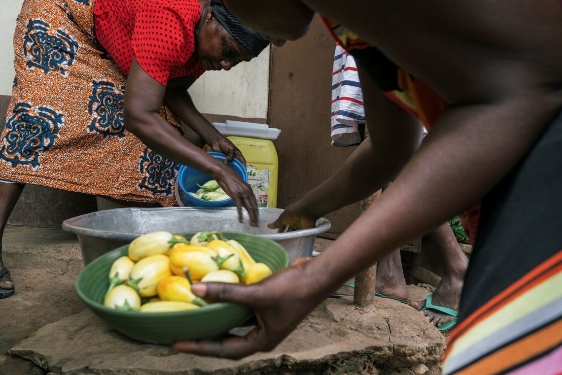 Grace, a maize farmer in Ghana, stands over a bowl with members of her family.