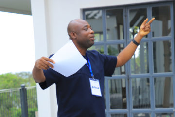 Alfred Yeboah stands outside in the center of a courtyard while facilitating Grameen's Power Dynamics Workshop