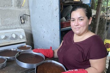 A woman stands at her oven holding two round pans with fresh-baked banana bread