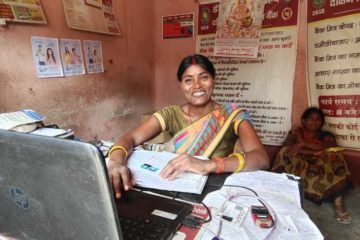 Malti, a Community Agent in Bihar, India, sits at her desk with a laptop. She is smiling at the camera.
