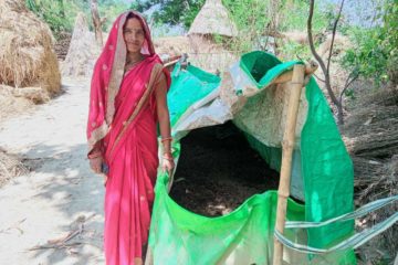 A woman stands next to a large green bag of soil