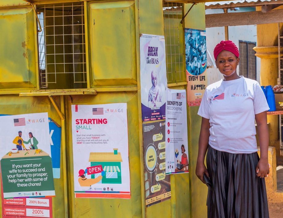 A DFS+ Grameen Agent in Ghana stands next to her kiosk