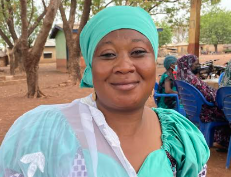 Sadia, a Grameen Agent in Ghana. She's sitting in a chair, wearing a turquoise headscarf and dress.
