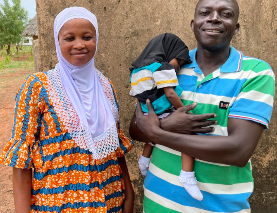 Sarita, a Grameen Agent in Ghana, stands with her husband Yussif. Yussif is holding their infant child.